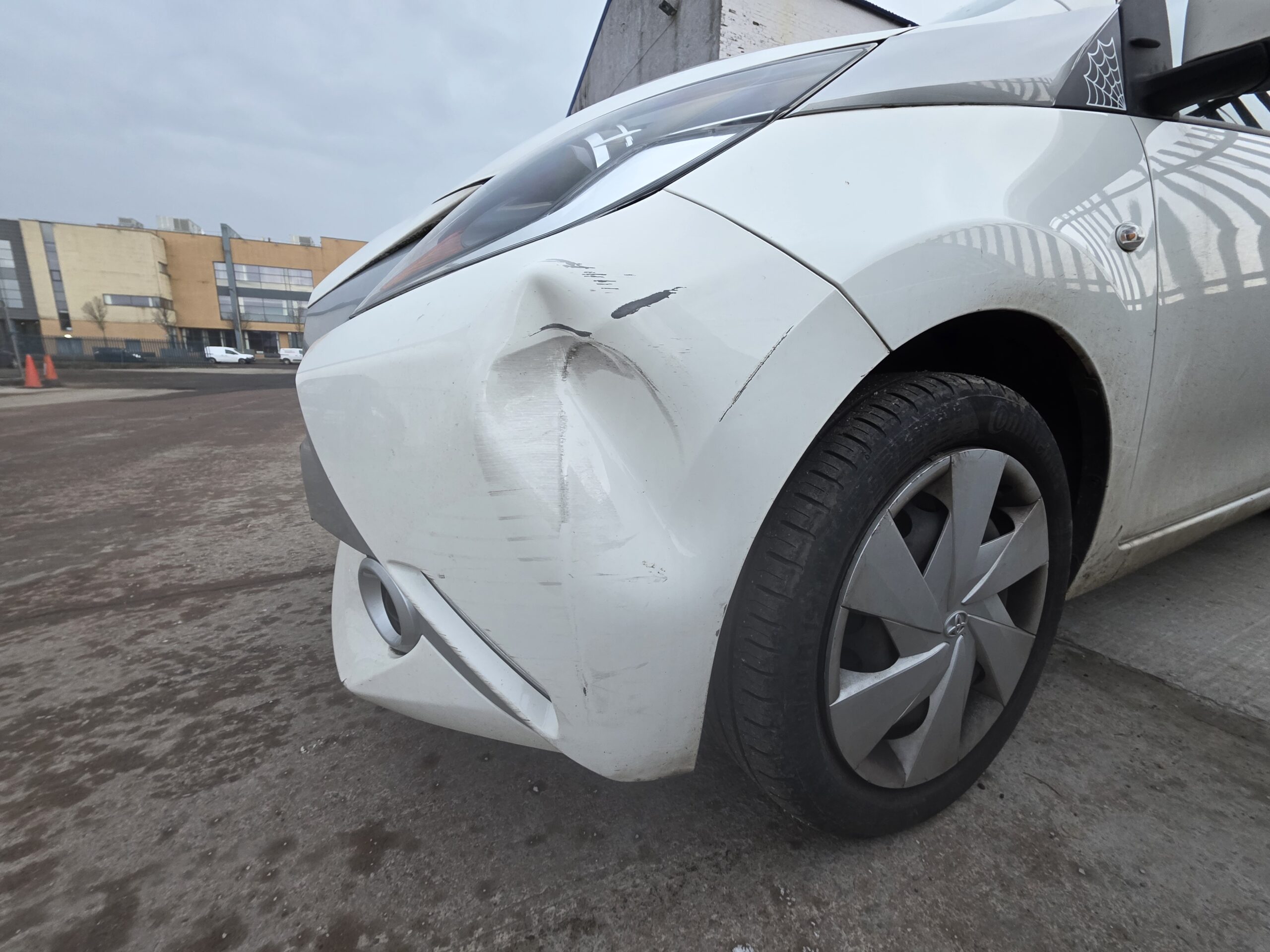 White Toyota with front corner collision damage in the Linwood Coachworks yard, Paisley
