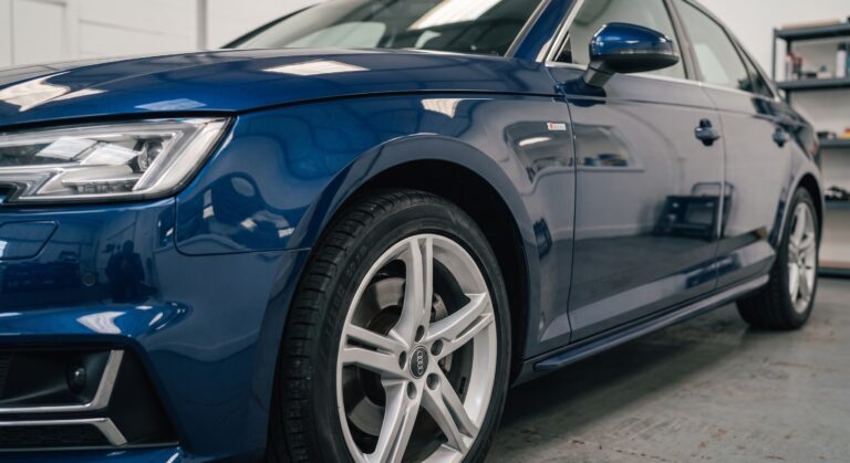 A professional, front-quarter view of a deep blue Audi sedan within the clean environment of Linwood Coachworks bodyshop, highlighting the front grille